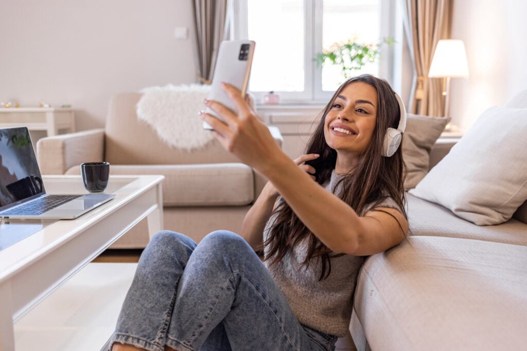 Close up of a young lady using her phone to listen to music. Beautiful young woman listening music and taking selfie. Selfie of a young woman listening to the music and enjoying at home.